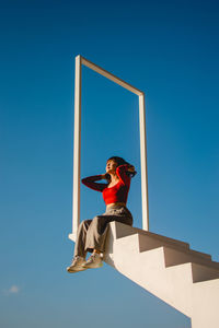 Low angle view of boy against blue sky on sunny day