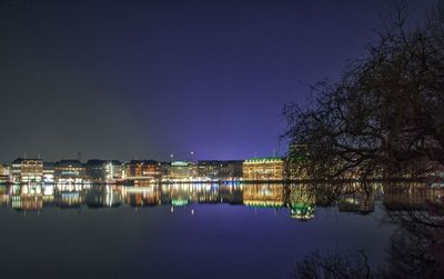 Illuminated buildings by lake against clear blue sky at night