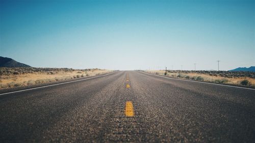 Road passing through landscape against clear blue sky