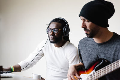 Man playing guitar while friend listening through headphones