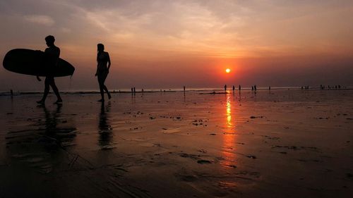 Silhouette man carrying surfboard walking with woman at beach during sunset