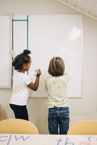 Rear view of boy and girl writing on whiteboard in elementary school