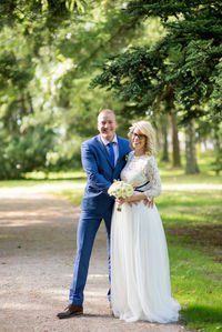 Full length portrait of bride and bridegroom standing on footpath at park