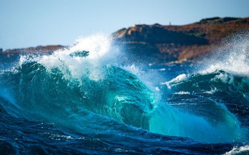 Sea waves splashing on shore against sky