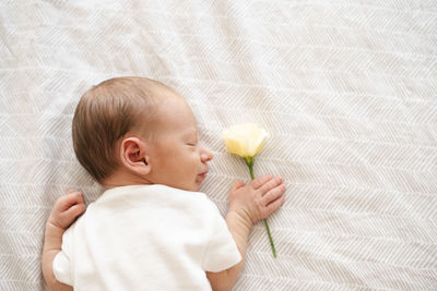 Cute newborn baby boy sleeping on bed at home holding flower