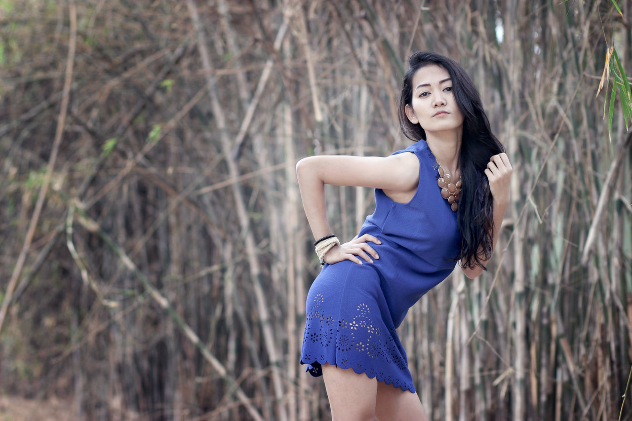 PORTRAIT OF YOUNG WOMAN WITH ARMS OUTSTRETCHED STANDING AGAINST TREES