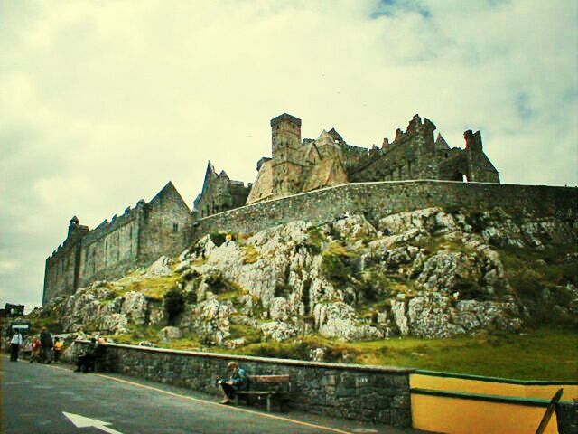 transportation, sky, car, land vehicle, architecture, built structure, road, cloud - sky, mountain, building exterior, mode of transport, cloud, street, rock formation, cloudy, travel, rock - object, incidental people, outdoors, day