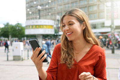 Close-up of happy casual woman watching smartphone screen in alexanderplatz square in berlin,germany