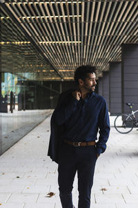 Smiling businessman holding blazer while walking in city