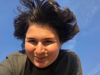 Close-up portrait of woman smiling against blue sky