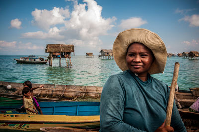 Smiling woman wearing hat and holding cane while in boat on sea against sky