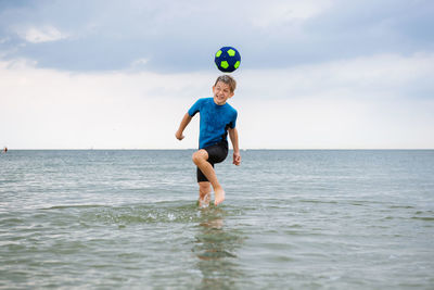 Cheerful boy playing with ball in sea
