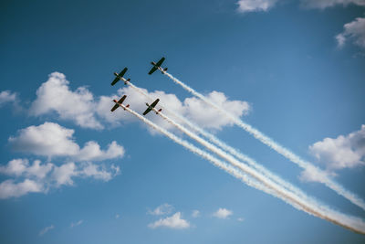 Low angle view of airplanes flying against cloudy sky during sunny day