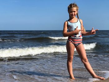 Smiling girl standing on shore at beach against sky during sunny day