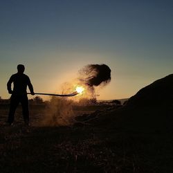 Silhouette man throwing dirt on field during sunset