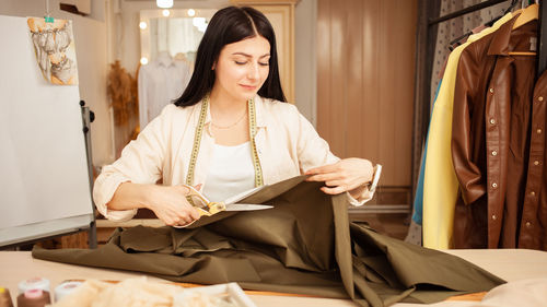 Black haired seamstress in atelier, portrait at work. table with fabric and sewing tools, 