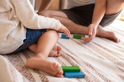 Low section of father and daughter playing with toy blocks on bed at home