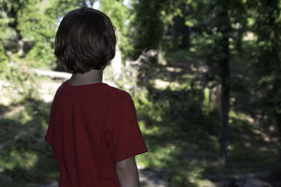 Boy standing against trees in forest