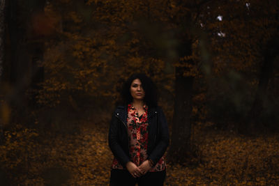 Portrait of beautiful woman standing by tree during autumn