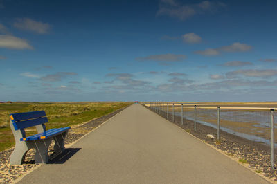 Empty deck chairs by sea against sky