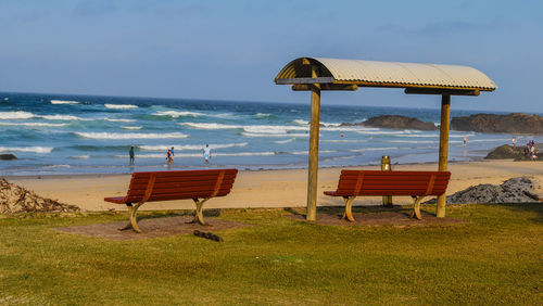 Deck chairs on beach against sky