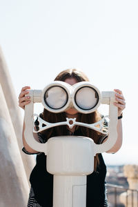 Close-up of woman looking through binoculars against clear sky
