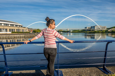 Woman standing on footbridge over river in city