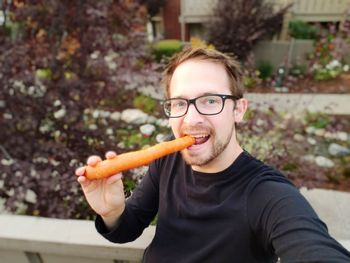 Portrait of man eating carrot while standing at park