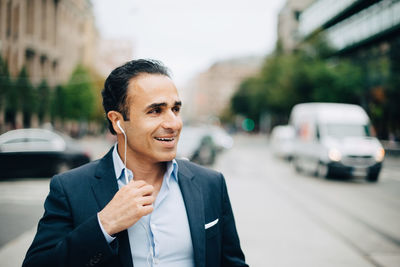 Smiling mature businessman talking through headphones while walking in city