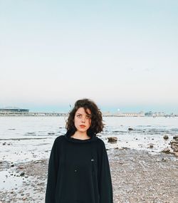 Portrait of beautiful young woman standing at beach against sky