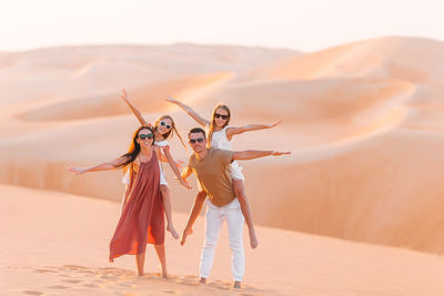 Portrait of parents with arms outstretched piggybacking daughters at desert