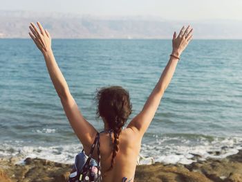 Rear view of woman with arms raised standing against sea