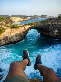 Low section of people on rock by sea against sky