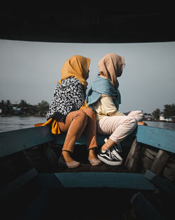 Rear view of couple sitting on shore against sky