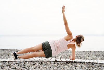 Young woman with arms raised on beach against sky