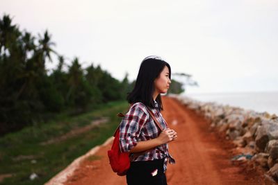 Young woman looking away while standing on land against sky