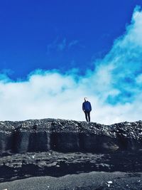 Man standing on rock against blue sky