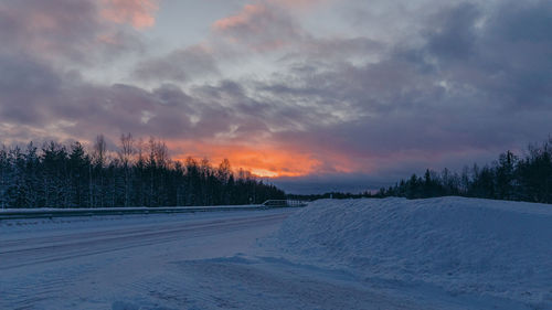 Snow covered landscape against sky during sunset