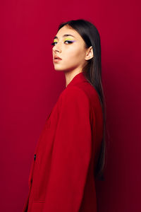 Portrait of young woman standing against red background