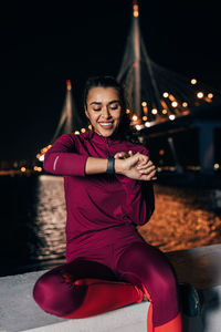 Smiling young woman sitting on illuminated bridge at night