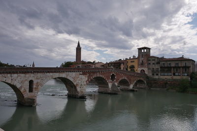 Arch bridge over river by buildings against sky