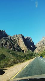 Country road leading towards mountains against blue sky