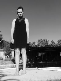 Portrait of woman standing by swimming pool against clear sky