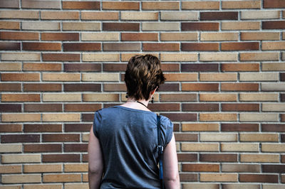 Rear view of woman standing against brick wall