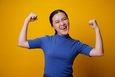 Portrait of smiling young woman against yellow background