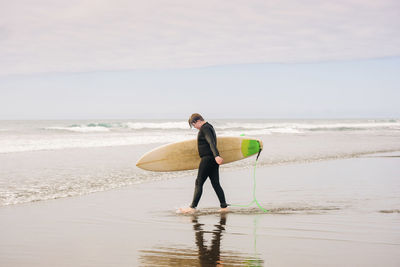 Boy walking into the water holding a surfboard at the beach