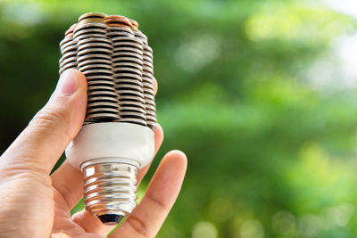 Cropped hand of man holding light bulb against plants