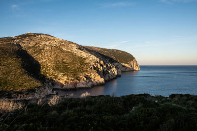 Scenic view of rocks by sea against sky