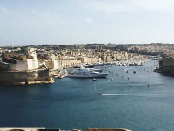 Boats in river by buildings against sky on sunny day in city