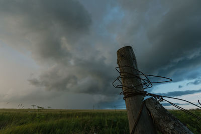 View of wooden post on field against storm clouds